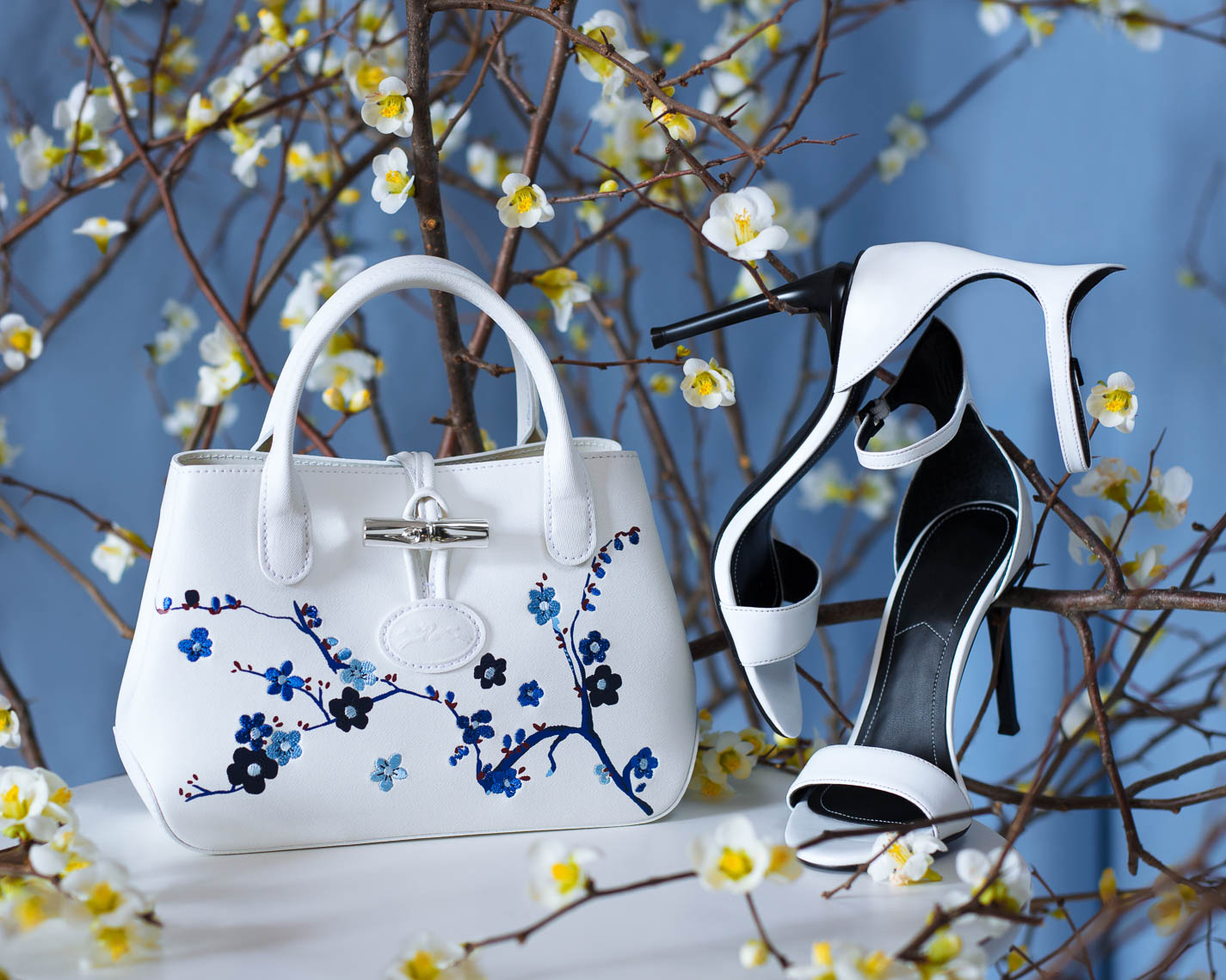 White leather handbag with high heel shoes and white flowers on a light blue background